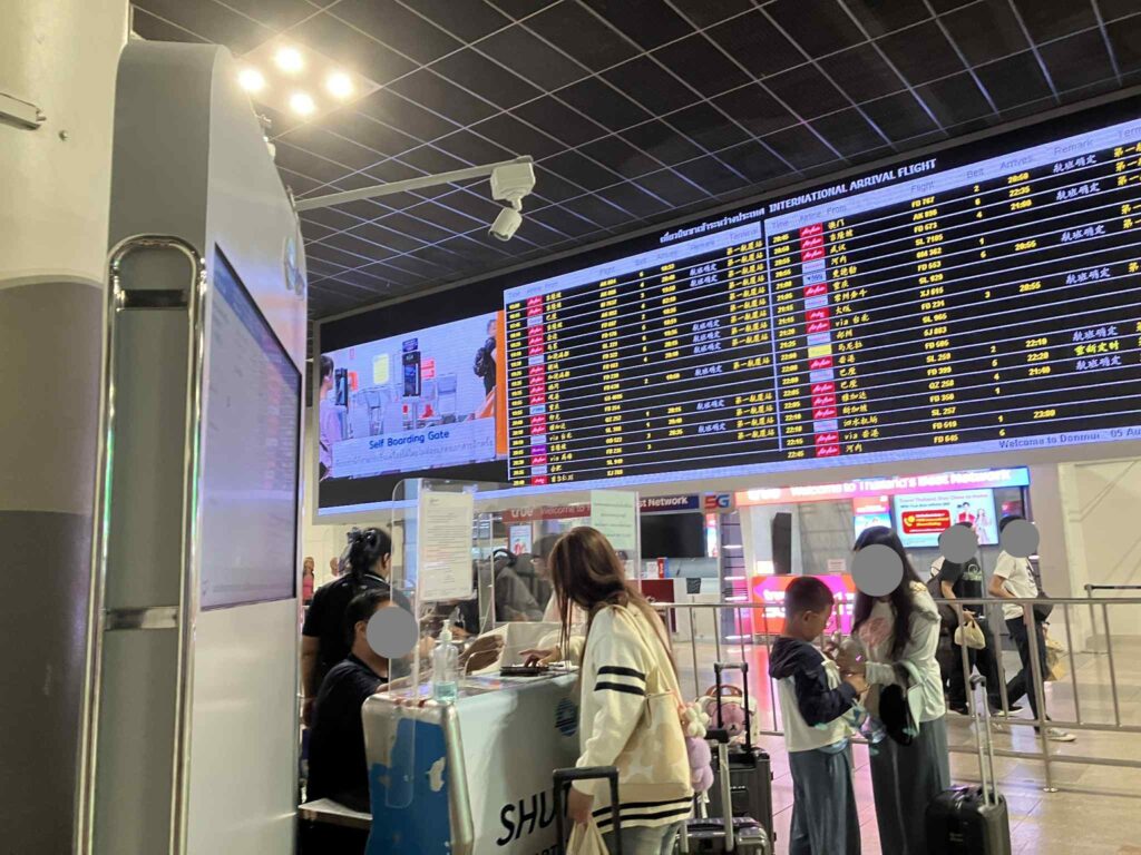 国際線到着便の大型フライト案内板（電光掲示板）前のシャトルバス受付