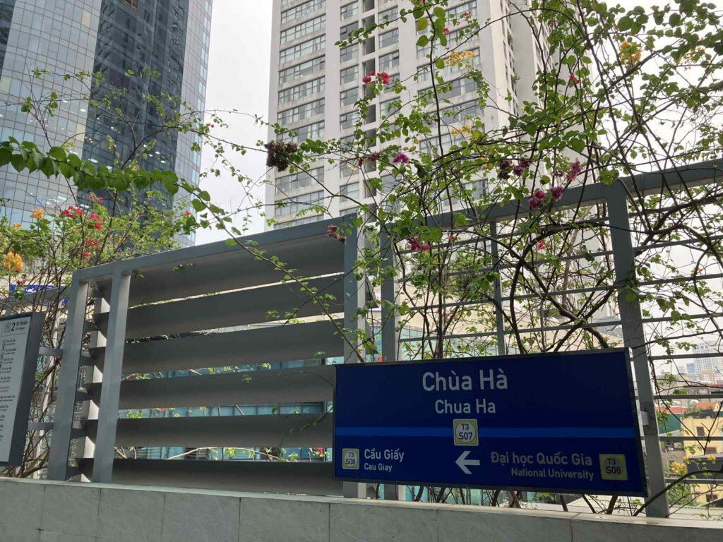 Chùa Hà駅の駅名サインと後ろに聳え立つ高層ビル。