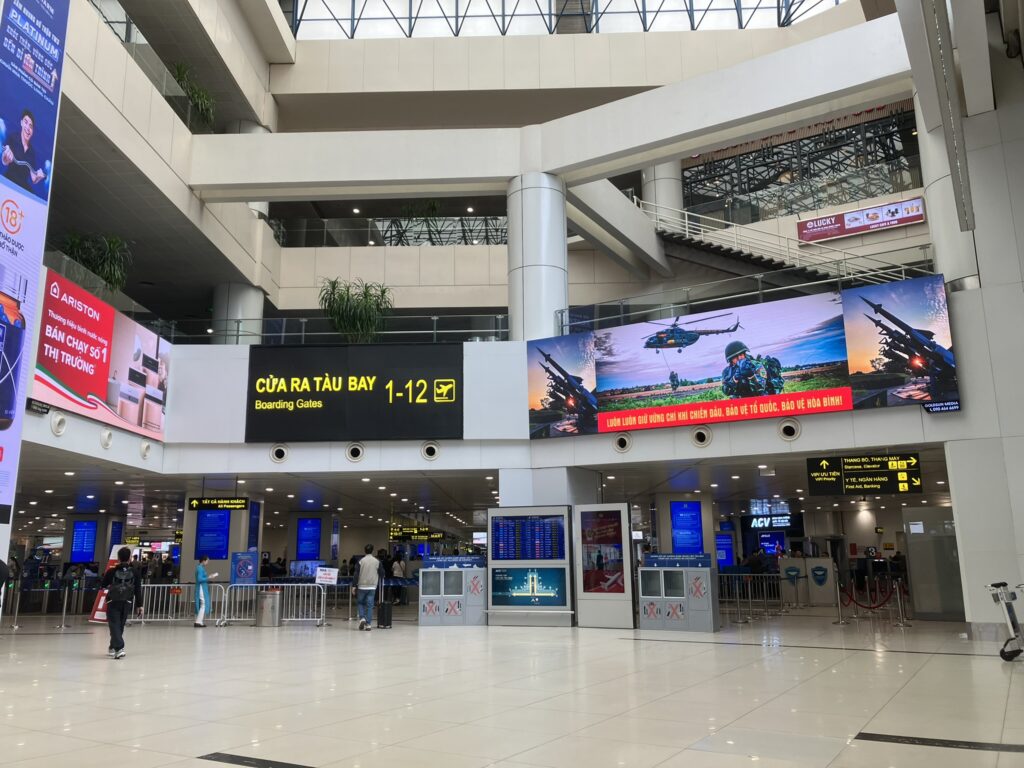 ノイバイ空港T1で搭乗ゲート1〜12へ向かう通路。ガラス越しに駐機場が見え、出発エリアまでの動線が分かりやすい。